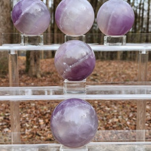 May include: Five amethyst crystal spheres on clear acrylic stands. The spheres are various shades of purple and white.