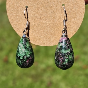 May include: A pair of silver dangle earrings with green and pink teardrop-shaped stones. The stones have a mottled pattern.