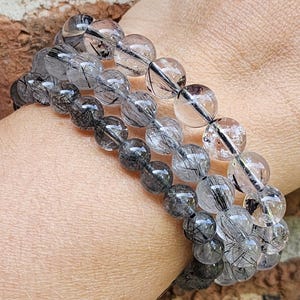 May include: A set of four bracelets made with clear quartz beads containing black inclusions. The beads are round and have a smooth, polished finish.