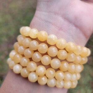 May include: A stack of yellow gemstone bracelets with round beads. The bracelets are made of natural stones and are worn on a person's wrist.