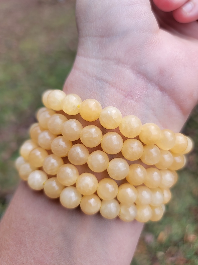 May include: A stack of yellow gemstone bracelets with round beads. The bracelets are made of natural stones and are worn on a person's wrist.