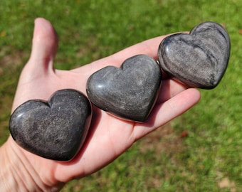 May include: Three black and grey heart-shaped stones. The stones have a swirling pattern and are smooth and polished.