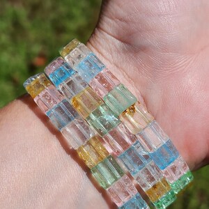 May include: Three stacked bracelets made of colorful, translucent, square-shaped beads. The beads are a mix of light blue, green, pink, and yellow.