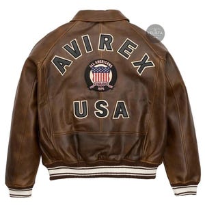 May include: Brown leather jacket with the word "AVIREX" across the back in white lettering. Below the word "AVIREX" is a patch with the words "ALL AMERICANS ESTABLISHED 1975" and a USA flag. The word "USA" is below the patch. The jacket has white and brown striped cuffs.