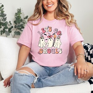 May include: A pink t-shirt with a graphic of three ghosts and the text "Let's Go Ghouls" in a retro font.