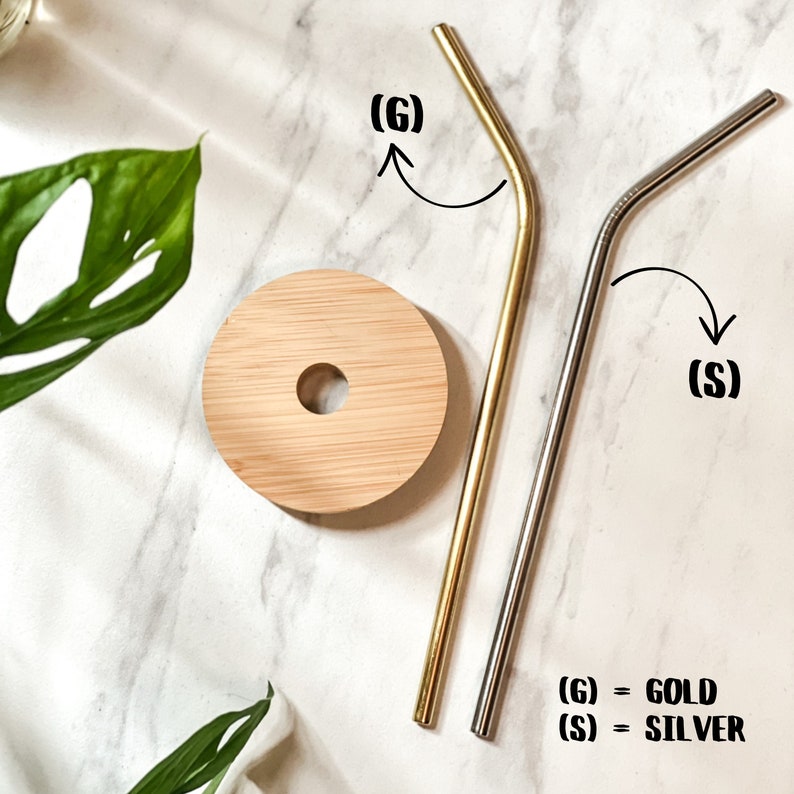 May include: Two reusable drinking straws, one gold and one silver, on a white marble surface. The straws are bent at a 90-degree angle. The text (G) = GOLD and (S) = SILVER is visible below the straws.