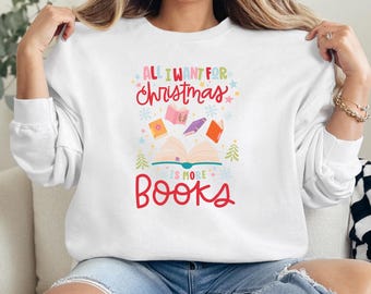 May include: White sweatshirt with a colourful graphic design featuring the text "All I want for Christmas is more books". The graphic includes a stack of books with snowflakes and a Christmas tree.