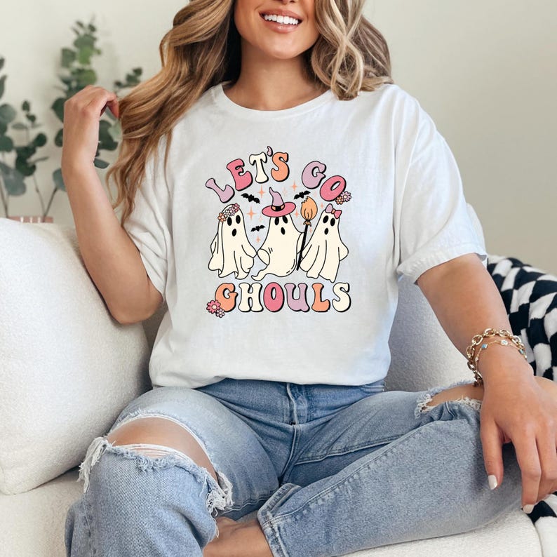 May include: White t-shirt with a graphic of three ghosts and the text "Let's Go Ghouls" in pink and orange letters.