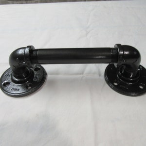 May include: Black metal pipe handle with two flanges. The handle is approximately 30 cm long.