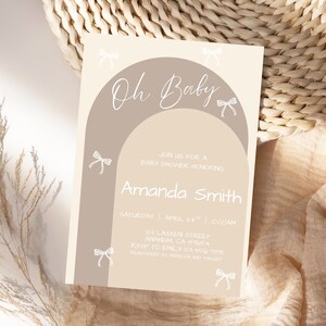 May include: A baby shower invitation in beige and taupe. The design features an arch shape with the words "Oh Baby" in script. The invitation includes details for Amanda Smith's baby shower, including the date, time, and location.
