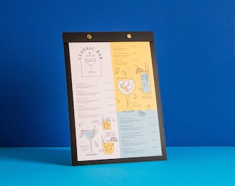 Puede incluir: Una pizarra negra con fondo blanco y detalles dorados. La pizarra tiene una lista de bebidas y precios, incluyendo Gin & Tonic, Old Fashioned y Margarita. La pizarra también tiene ilustraciones de cócteles.