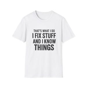 Op de afbeelding: Wit t-shirt met de tekst "THAT'S WHAT I DO I FIX STUFF AND I KNOW THINGS" in zwarte blokletters. Het shirt heeft een ronde hals en korte mouwen. De tekst is gecentreerd op de voorkant van het shirt.