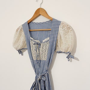 Puede incluir: Un vestido de cuadros azules y blancos con un corpi&ntilde;o de encaje blanco y mangas abullonadas. El vestido tiene un lazo en la cintura.