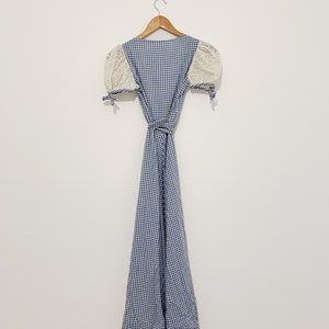 Puede incluir: Un vestido de cuadros vichy azul y blanco con mangas de crochet blanco y un cintur&oacute;n de lazo.