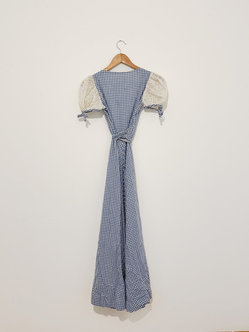 Puede incluir: Un vestido de cuadros vichy azul y blanco con mangas de crochet blanco y un cintur&oacute;n de lazo.