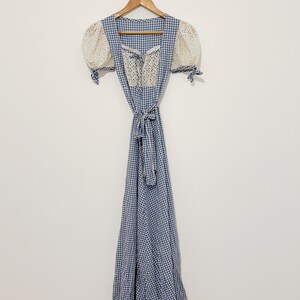Puede incluir: Un vestido de cuadros vichy azul y blanco con un corpi&ntilde;o de encaje blanco y mangas abullonadas. El vestido tiene un lazo en la cintura y una falda larga.