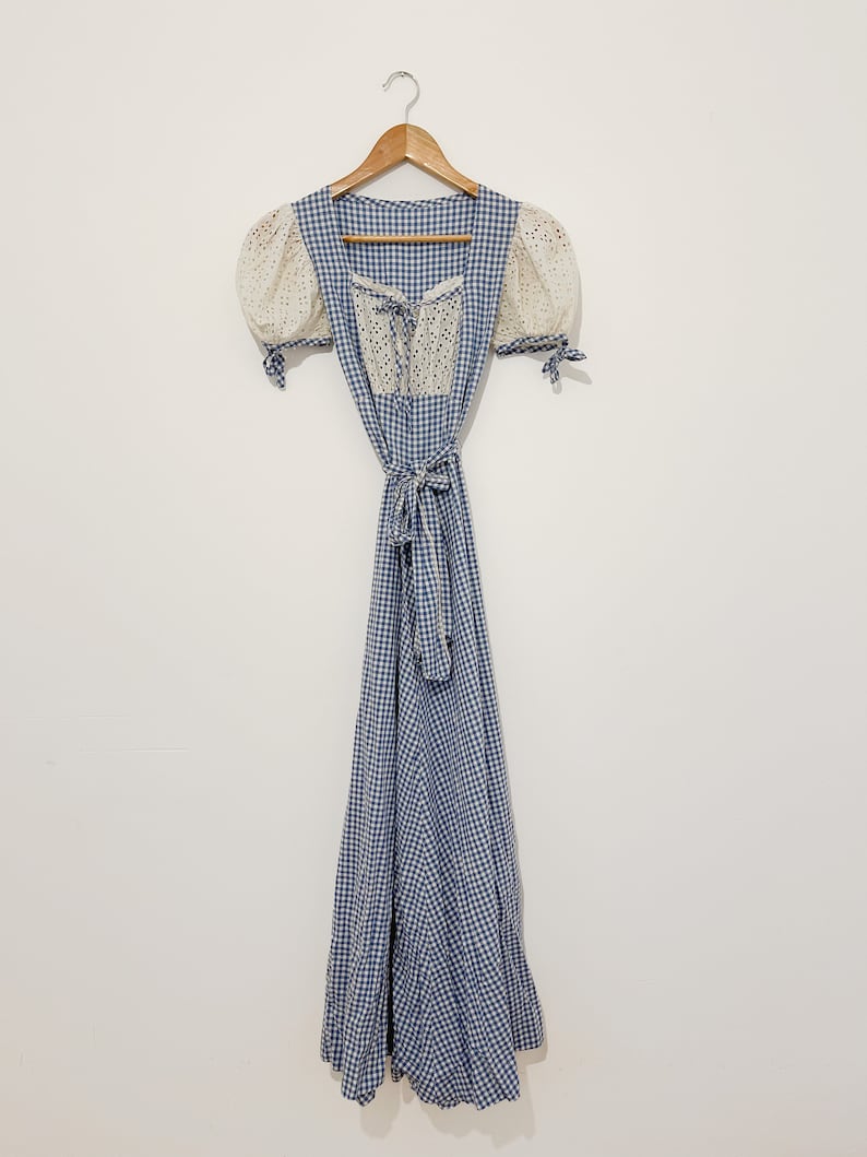 Puede incluir: Un vestido de cuadros vichy azul y blanco con un corpi&ntilde;o de encaje blanco y mangas abullonadas. El vestido tiene un lazo en la cintura y una falda larga.