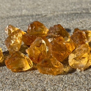 May include: A group of small, rough, orange-brown citrine crystals on a light grey surface.