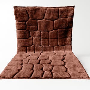 May include: A brown, textured bath mat with a stone-like pattern. The mat is rectangular with a raised, uneven surface, creating a visual of stacked stones. The color is a warm, earthy tone, suitable for a bathroom.