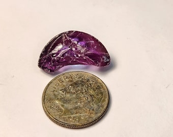 May include: A translucent, deep purple gemstone fragment next to a U.S. dime. The gemstone has a curved shape with visible internal fractures. The dime shows the word "LIBERTY" and the year 2021.