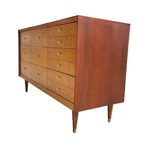 May include: A mid-century modern dresser with a light brown finish on the drawers and a darker brown finish on the sides. The dresser has multiple drawers with brass knobs and tapered legs.