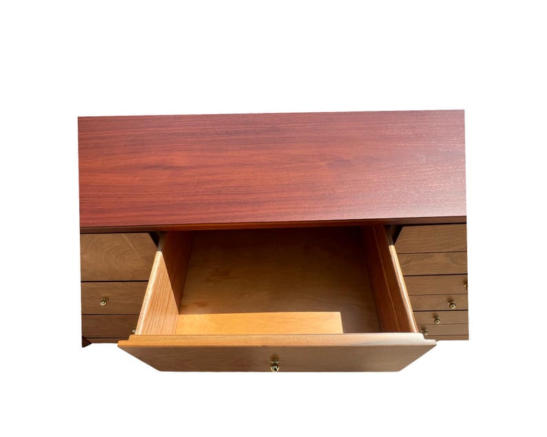 May include: A wooden desk with a dark reddish-brown top and a drawer pulled open. The drawer is made of light-colored wood and has a brass knob. Several other drawers are visible on the sides of the desk.