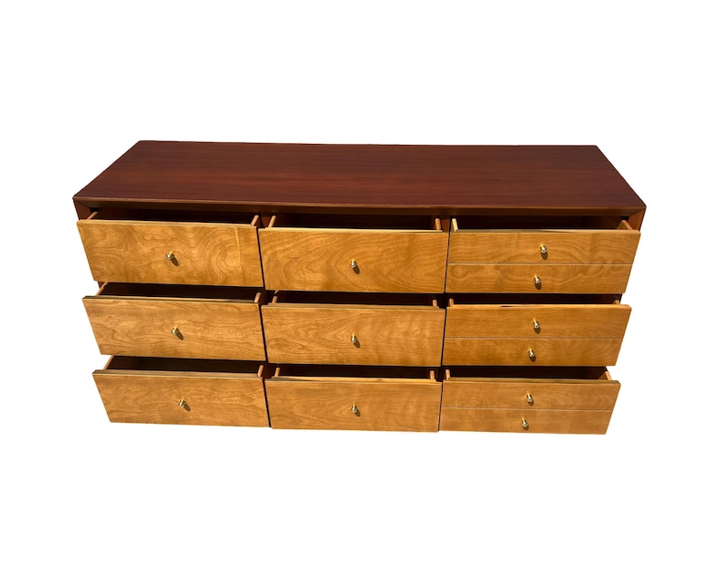May include: A mid-century modern dresser with nine drawers. The top is a dark brown, and the drawers are light wood with brass knobs. All drawers are open, revealing the interior.