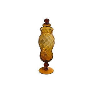 May include: A tall amber glass jar with a twisted design and a round lid. The jar has a wide base and a narrow neck.