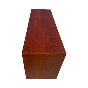 May include: A rectangular, wooden cabinet with a rich, reddish-brown finish. The cabinet has a simple, minimalist design with clean lines and a smooth surface. The wood grain is visible, adding texture and warmth to the piece.