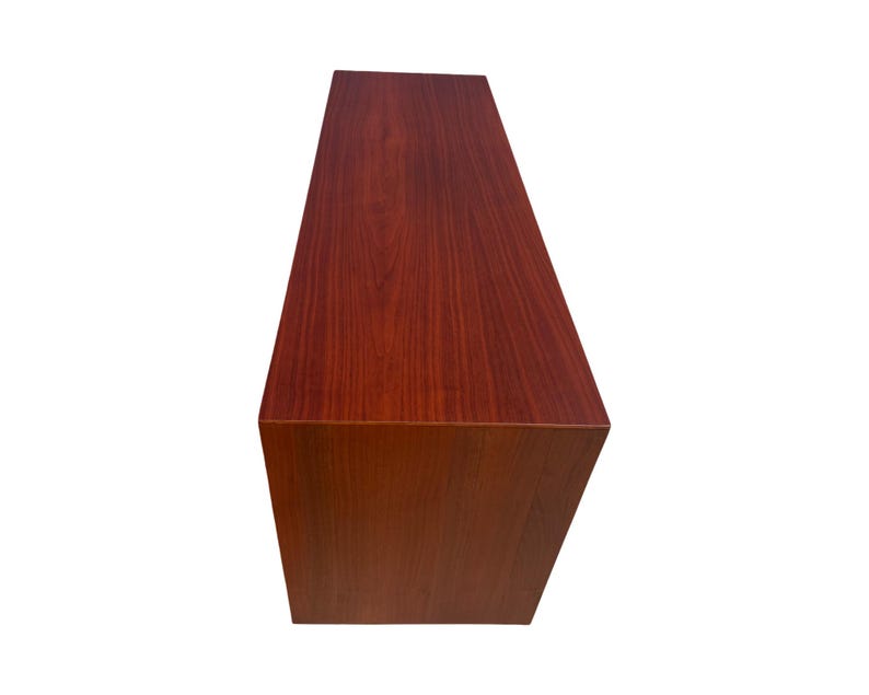 May include: A rectangular, wooden cabinet with a rich, reddish-brown finish. The cabinet has a simple, minimalist design with clean lines and a smooth surface. The wood grain is visible, adding texture and warmth to the piece.