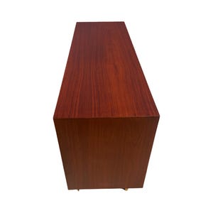 May include: A rectangular, wooden cabinet with a rich, reddish-brown finish. The cabinet has a simple, modern design with clean lines and a smooth surface. The wood grain is visible, adding texture and warmth to the piece.