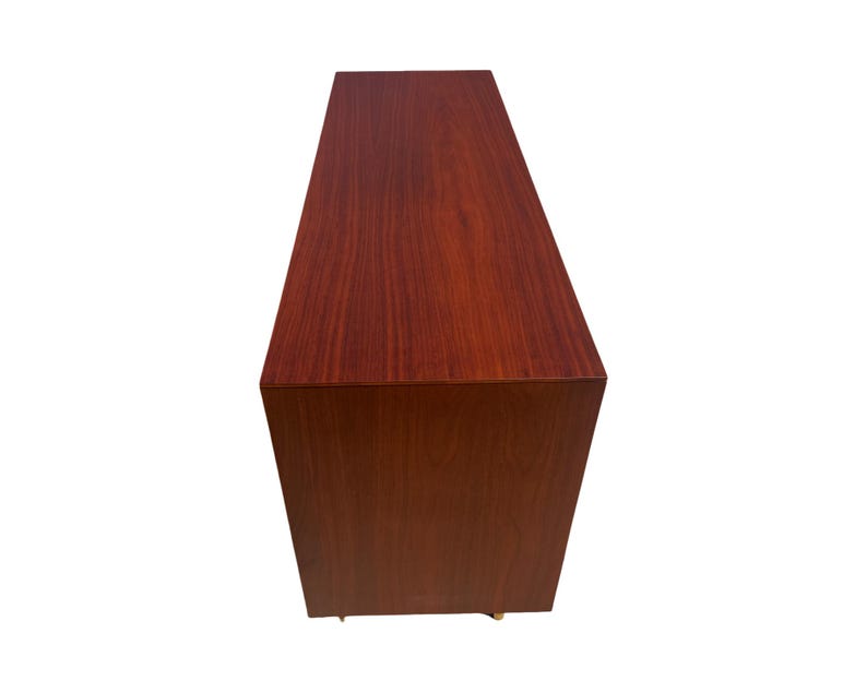 May include: A rectangular, wooden cabinet with a rich, reddish-brown finish. The cabinet has a simple, modern design with clean lines and a smooth surface. The wood grain is visible, adding texture and warmth to the piece.