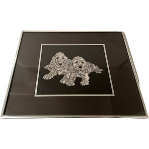 May include: A framed black and white illustration of two cocker spaniel puppies lying down on a black background.