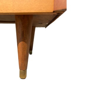 May include: A mid-century modern style wooden table with four tapered legs. The legs are a warm brown color with brass-colored metal tips. The table's underside is visible, showing its construction.