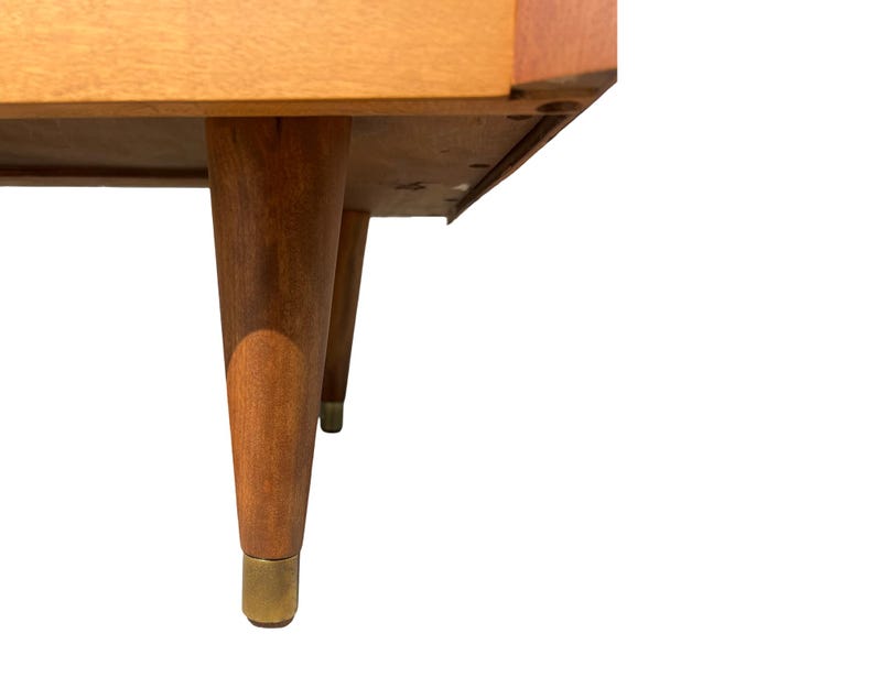 May include: A mid-century modern style wooden table with four tapered legs. The legs are a warm brown color with brass-colored metal tips. The table's underside is visible, showing its construction.