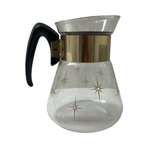 May include: A glass coffee pot with a black handle and a gold band around the top. The pot has a starburst pattern on the glass.