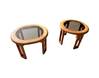 May include: Two wooden end tables with glass tops. One table has a round top and the other has an oval top.