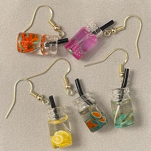 May include: A collection of five novelty earrings, each designed to resemble a miniature beverage in a clear plastic cup. The earrings feature gold-colored hooks and black straws. The drinks are various colors and include fruit slices.