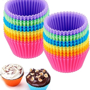 May include: A collection of vibrant silicone cupcake cases in shades of pink, yellow, green, blue, and purple. Two cupcakes are displayed, one with white frosting and sprinkles, the other with chocolate frosting and nuts. These reusable baking cups are ideal for baking.