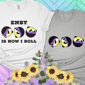 Puede incluir: Dos camisetas con un diseño de tres caras de panda. Las caras de panda están en los colores de la bandera del orgullo no binario. El texto en la camiseta blanca dice "ENBY IS HOW I ROLL".