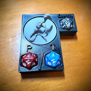 May include: A black 3D printed dice tray with a circular compartment for a miniature, two dice compartments labeled "P" and "T", and a compartment for a larger die labeled "Qwerty".