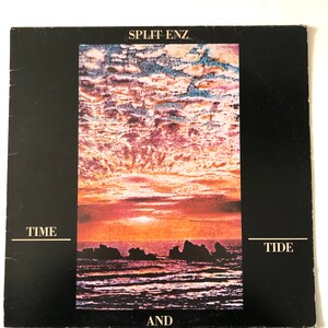 Peut inclure: Pochette d'album vinyle vintage de Split Enz, avec le titre "Time and Tide". L'illustration présente un coucher de soleil sur l'océan, avec un ciel coloré et des rochers sombres. Le fond est noir avec du texte blanc.