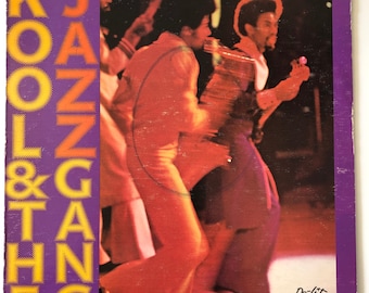 May include: Vintage vinyl record album cover for Kool & The Gang. The cover features a purple and orange design with the band's name in large, stylized letters. The image shows band members in orange and purple outfits.