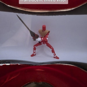 May include: A red action figure with a translucent tinted visor, holding a silver sword with a gold handle. The figure is wearing a gold chest piece and red armor.