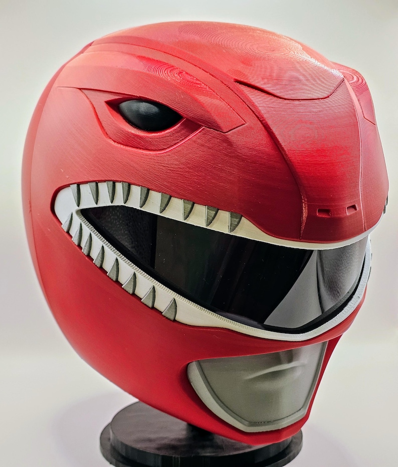 May include: A red plastic helmet with a white visor and a white, toothy mouth. The helmet has a black eye opening on each side.