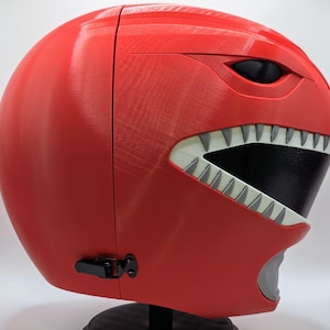 May include: Red plastic helmet with a white and black face mask and a white tooth design. The helmet has a black latch on the side.