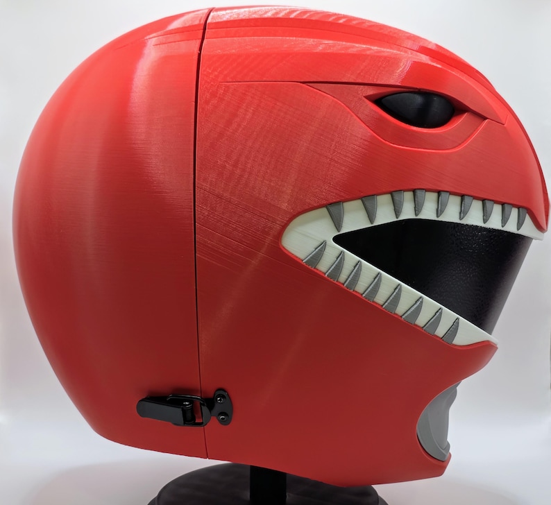 May include: Red plastic helmet with a white and black face mask and a white tooth design. The helmet has a black latch on the side.