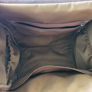 Puede incluir: El interior de una bolsa de pa&ntilde;ales de cuero marr&oacute;n con un bolsillo con cremallera y bucles el&aacute;sticos.