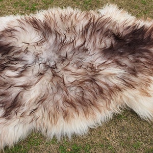 May include: A white sheepskin rug with brown and gray markings. The rug is soft and fluffy, and it would be perfect for adding a touch of warmth and comfort to any room.