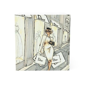 Op de afbeelding: Een vrouw in een witte jurk en jas loopt over een straat die aan beide kanten vol winkels staat. De winkels hebben borden met de tekst "Dior". Ze draagt ​​winkelzakken met hetzelfde logo.